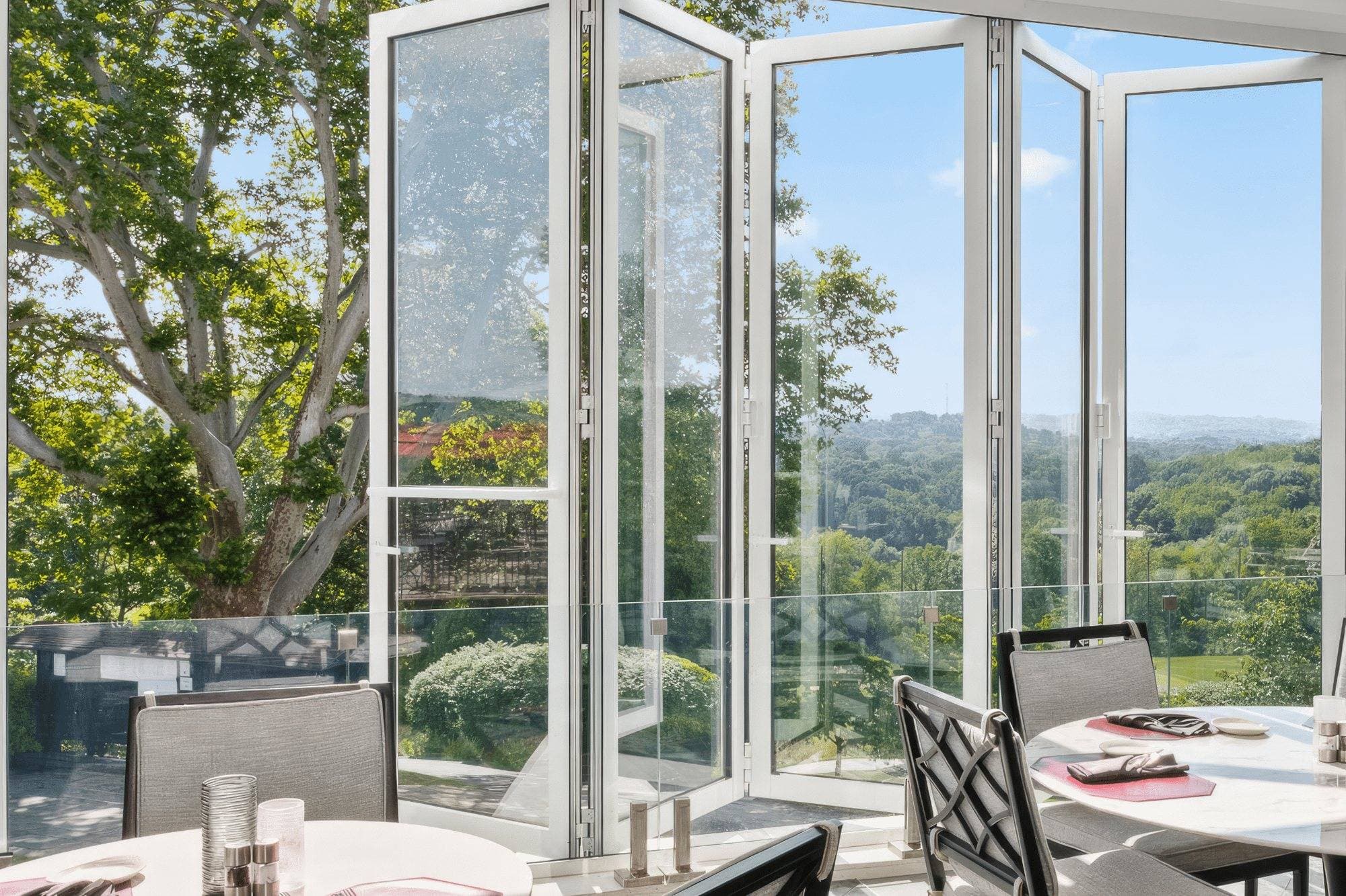 Euro-Wall Vista Fold folding glass wall with slim aluminum panels folded open in a bright dining room overlooking a wooded valley