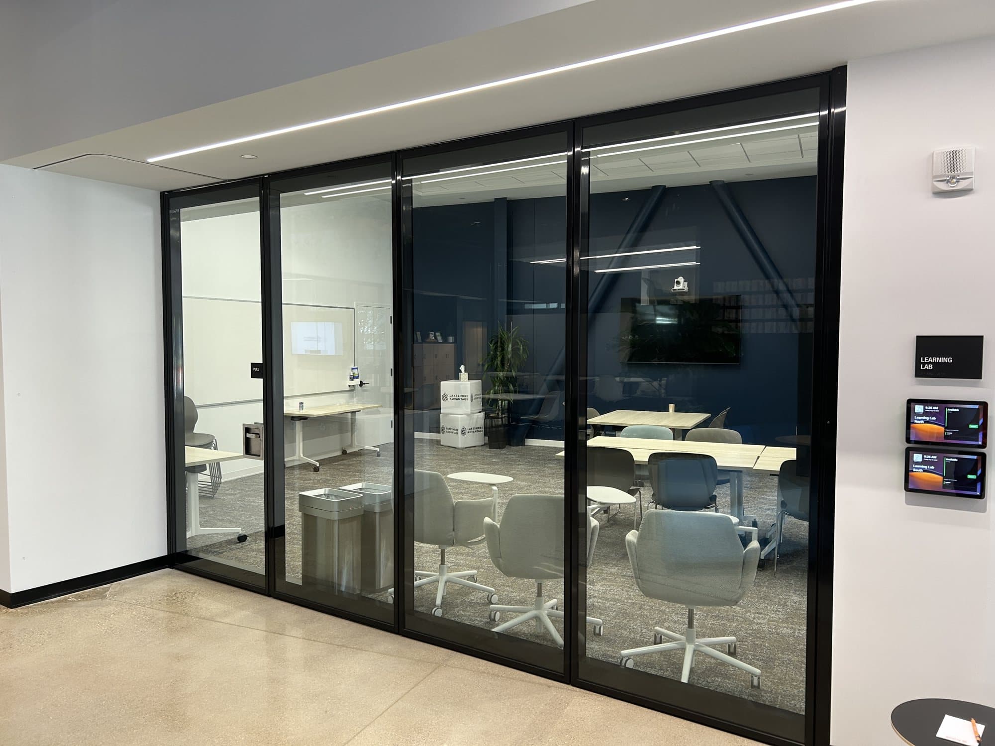 Fully closed black-framed Modernfold Acousti-Clear acoustical glass operable wall enclosing the Learning Lab meeting room off the lobby at Lakeshore Advantage