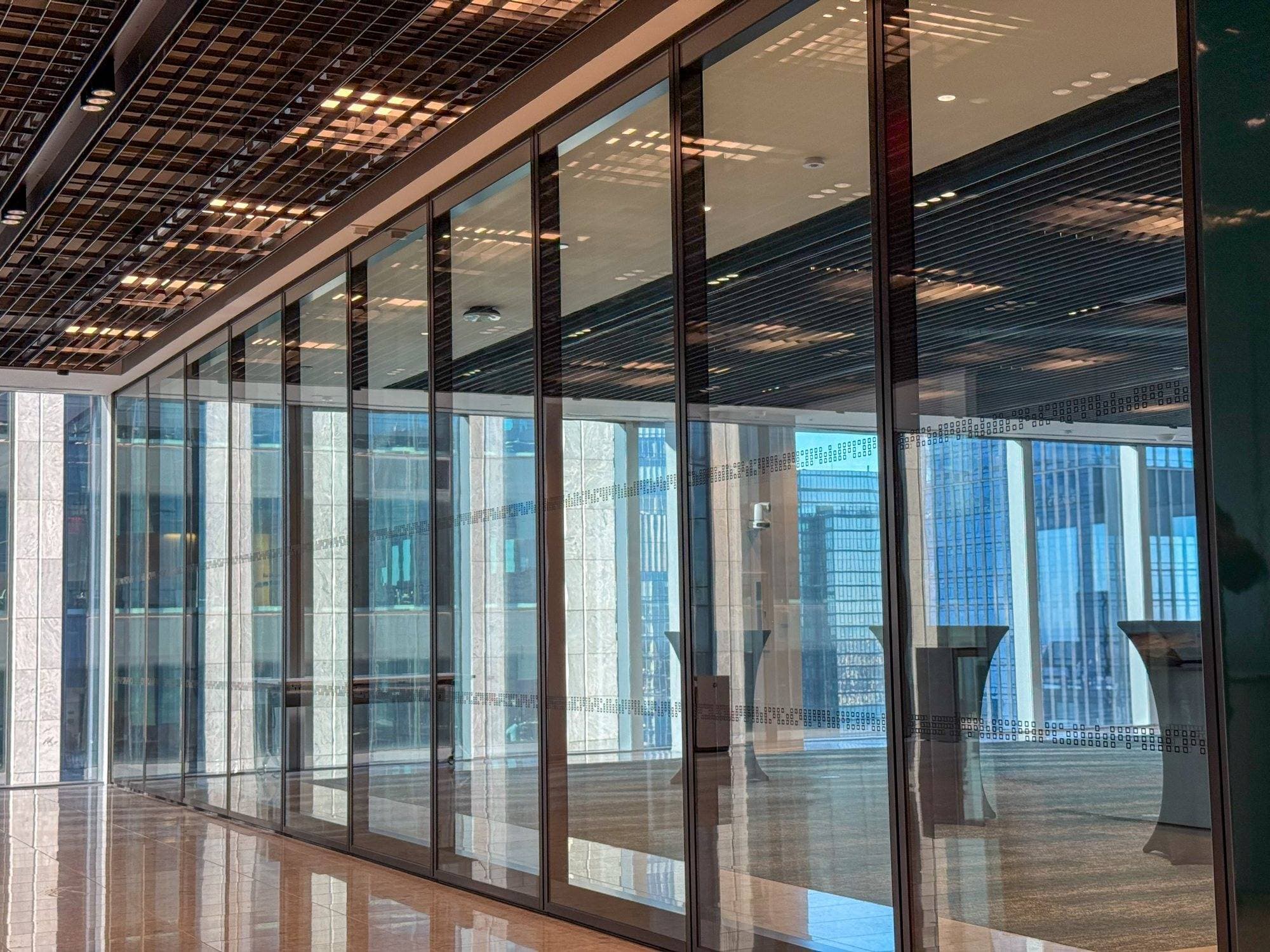 Closed Modernfold ComfortDrive automated glass operable wall at AllianceBernstein, a long black-framed glass run with a dotted privacy band in front of a skyline event space