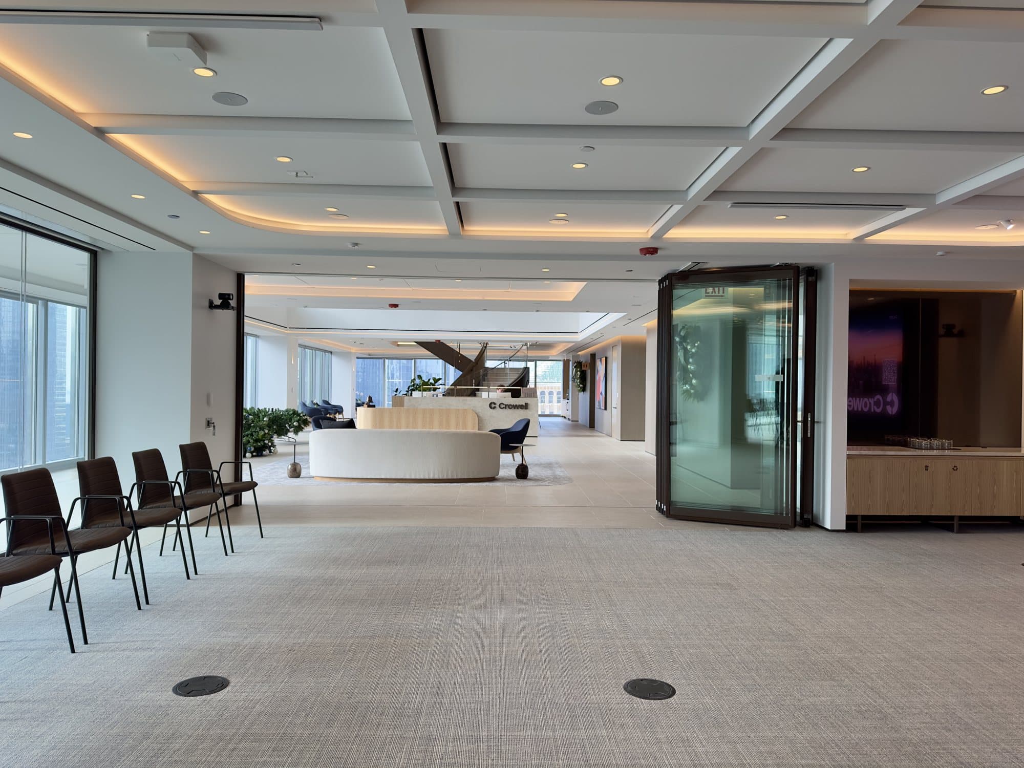 Modernfold ComfortDrive glass operable wall partly open at Crowell, with a single bronze-framed glass panel driving itself toward the stack and the reception area beyond