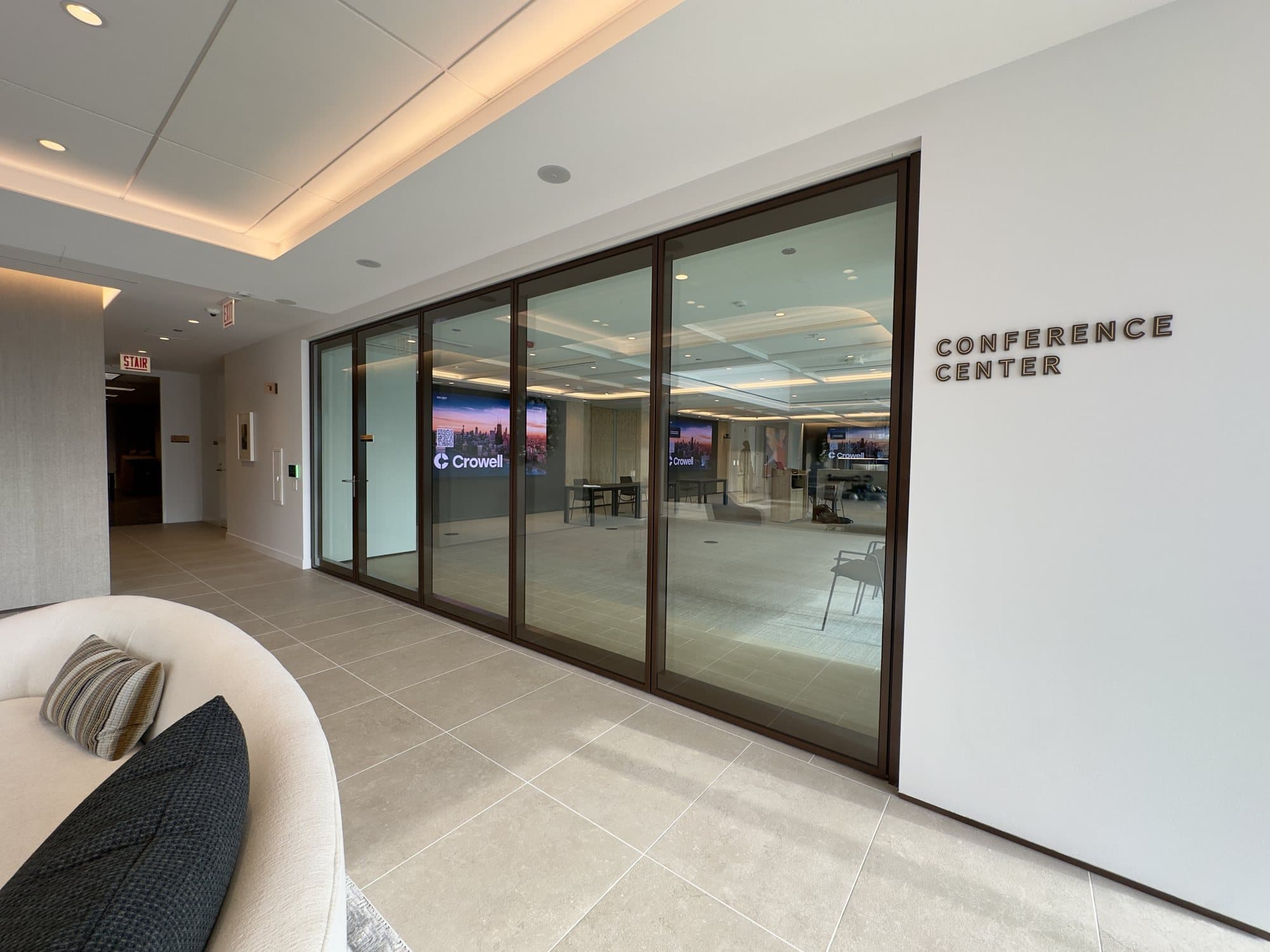 Closed Modernfold ComfortDrive automated glass operable wall with bronze frames at the entrance of the Crowell law firm conference center, beside Conference Center signage