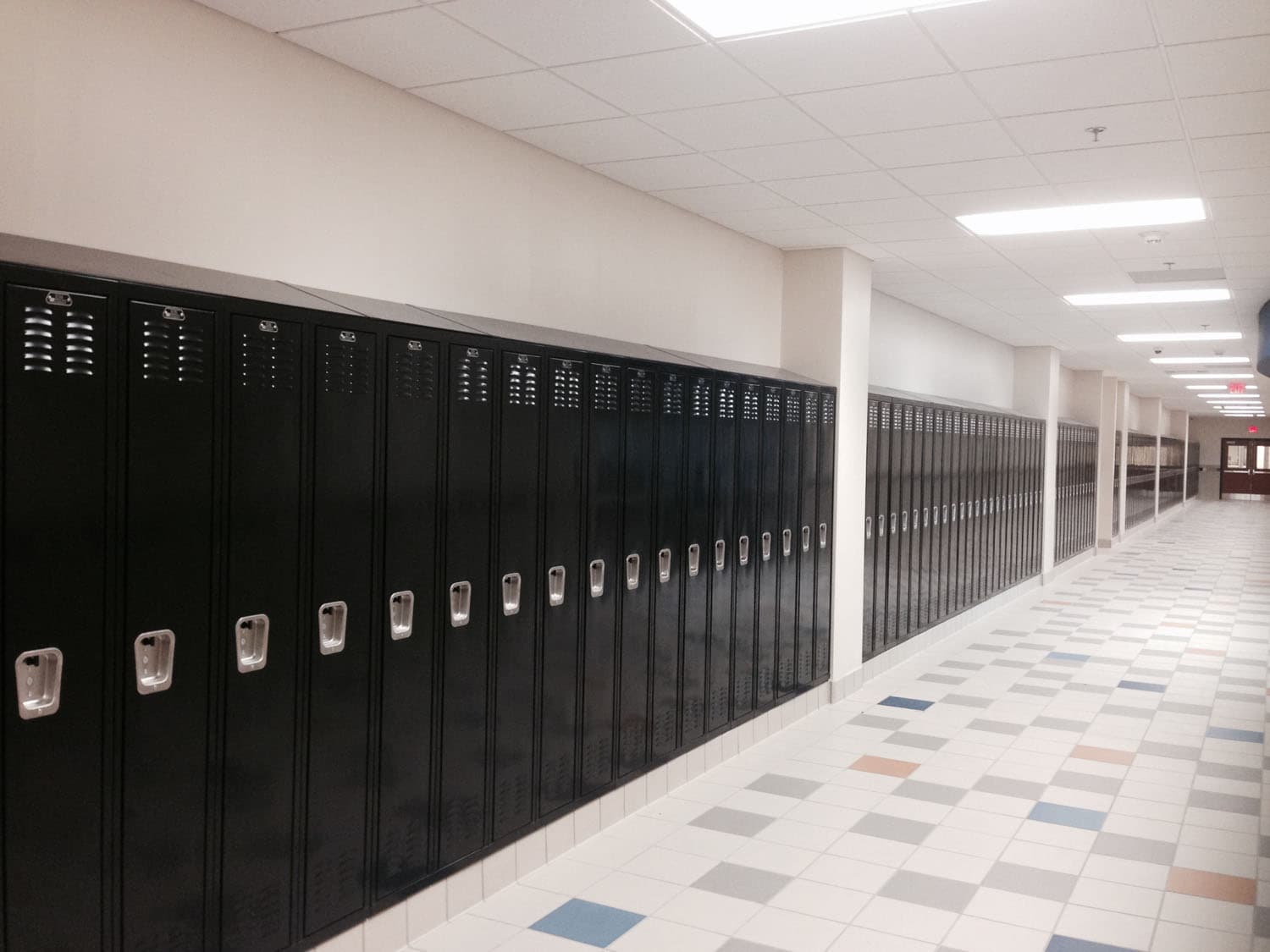 Long row of black List Industries metal lockers along a bright school corridor