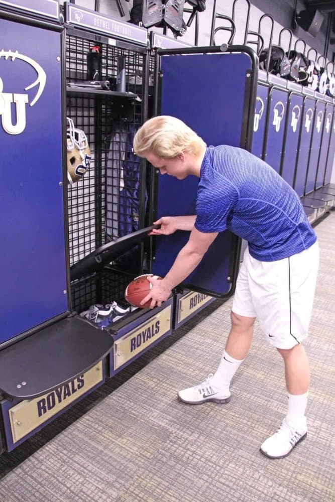 Athlete lifting the storage seat of a GearGrid wall mount team locker