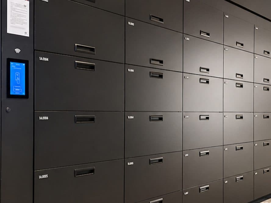 Bank of black laminate day-use lockers with a touchscreen access panel in an office corridor