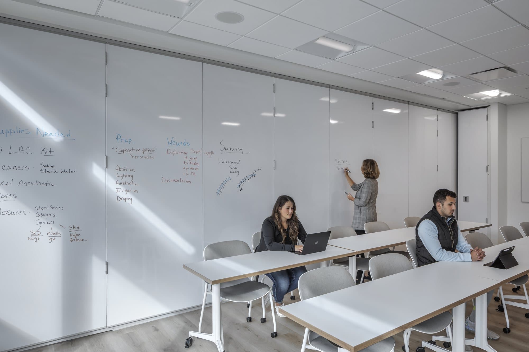 Fully closed Modernfold operable wall with writable markerboard panel faces in a Corewell Health nurse training classroom, students seated at tables
