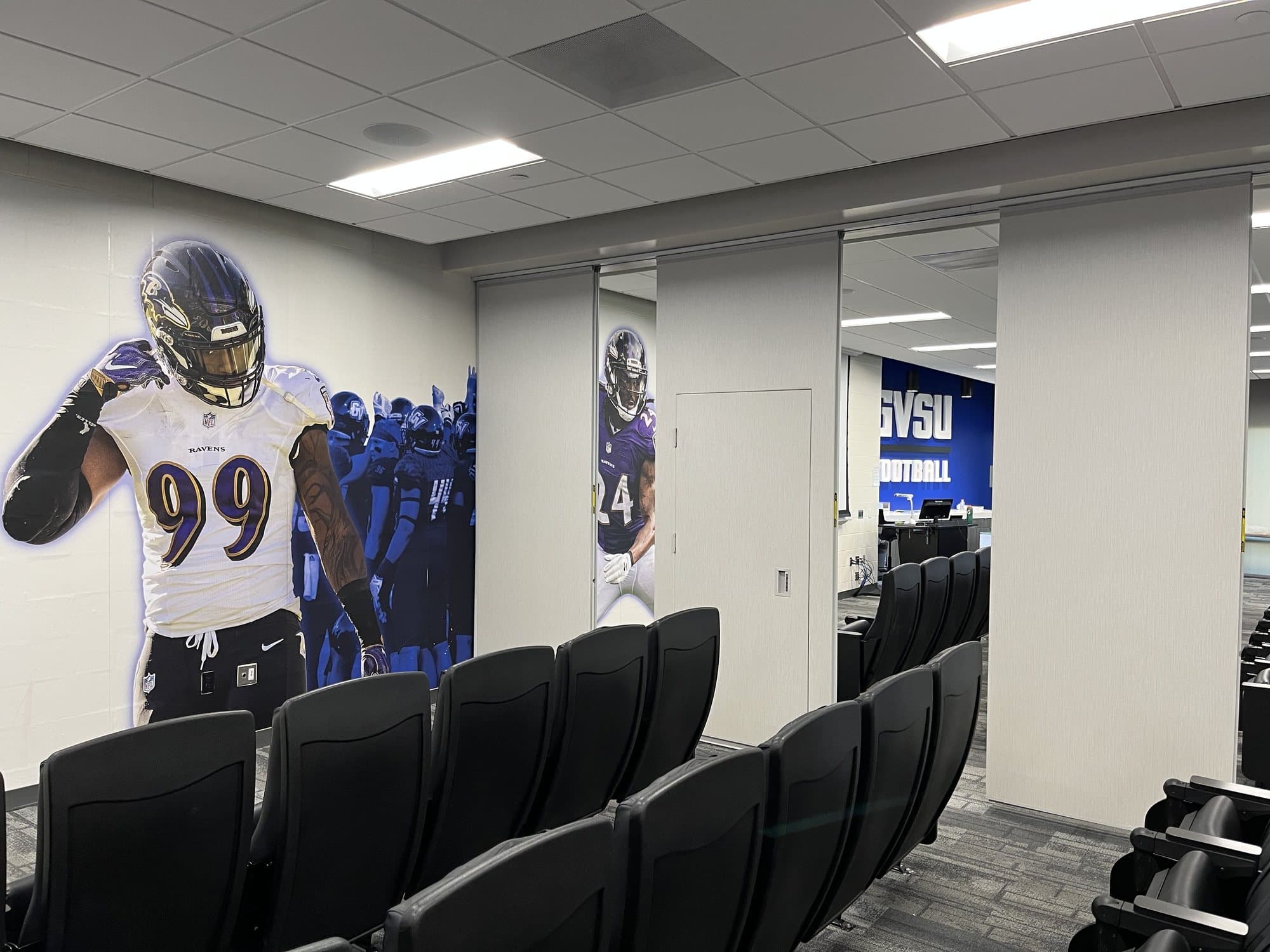 Modernfold folding panel partition partially open in the Grand Valley State University football film room, with theater seating and a pass door built into one panel