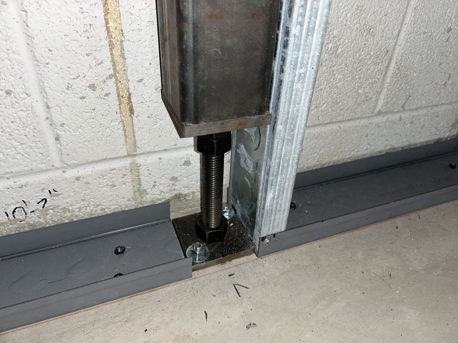 Steel truss post standing on an adjustable leveling leg and floor plate anchored to the concrete slab