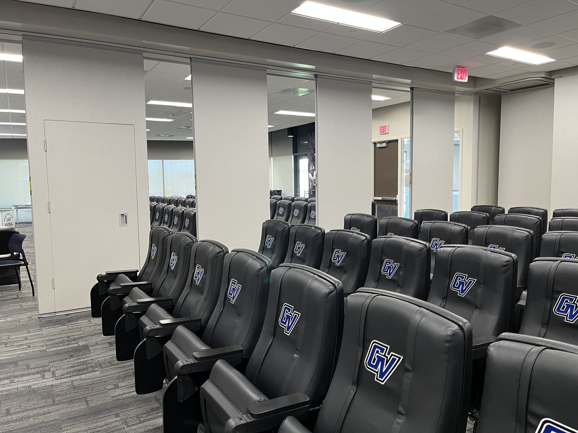 GVSU football film room with GV-logo theater seats and the Modernfold Acousti-Seal folding panel partition partly open, panels mid-stack