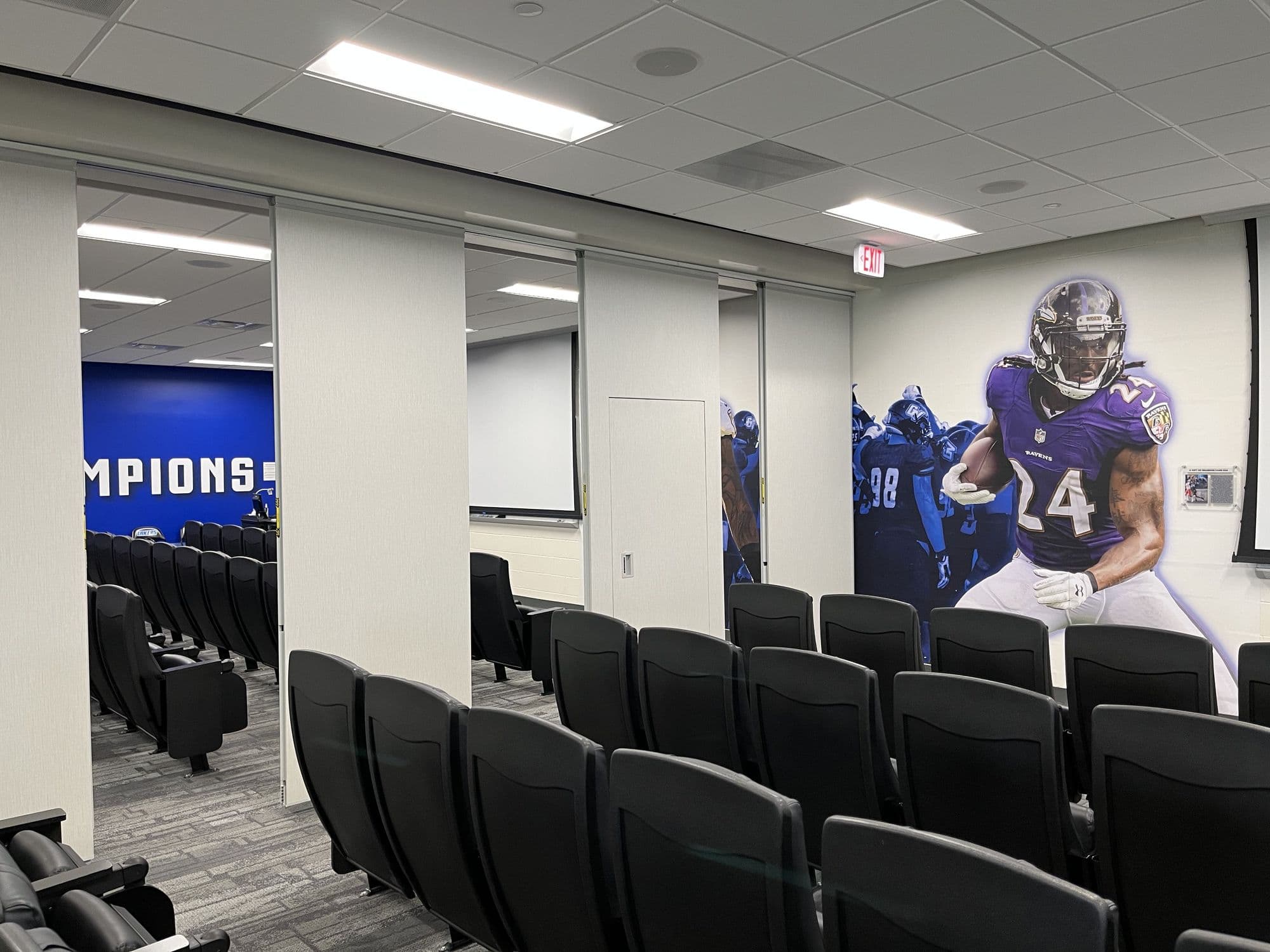 Partly open folding panel partition in the GVSU film room with a champions wall graphic and a player mural