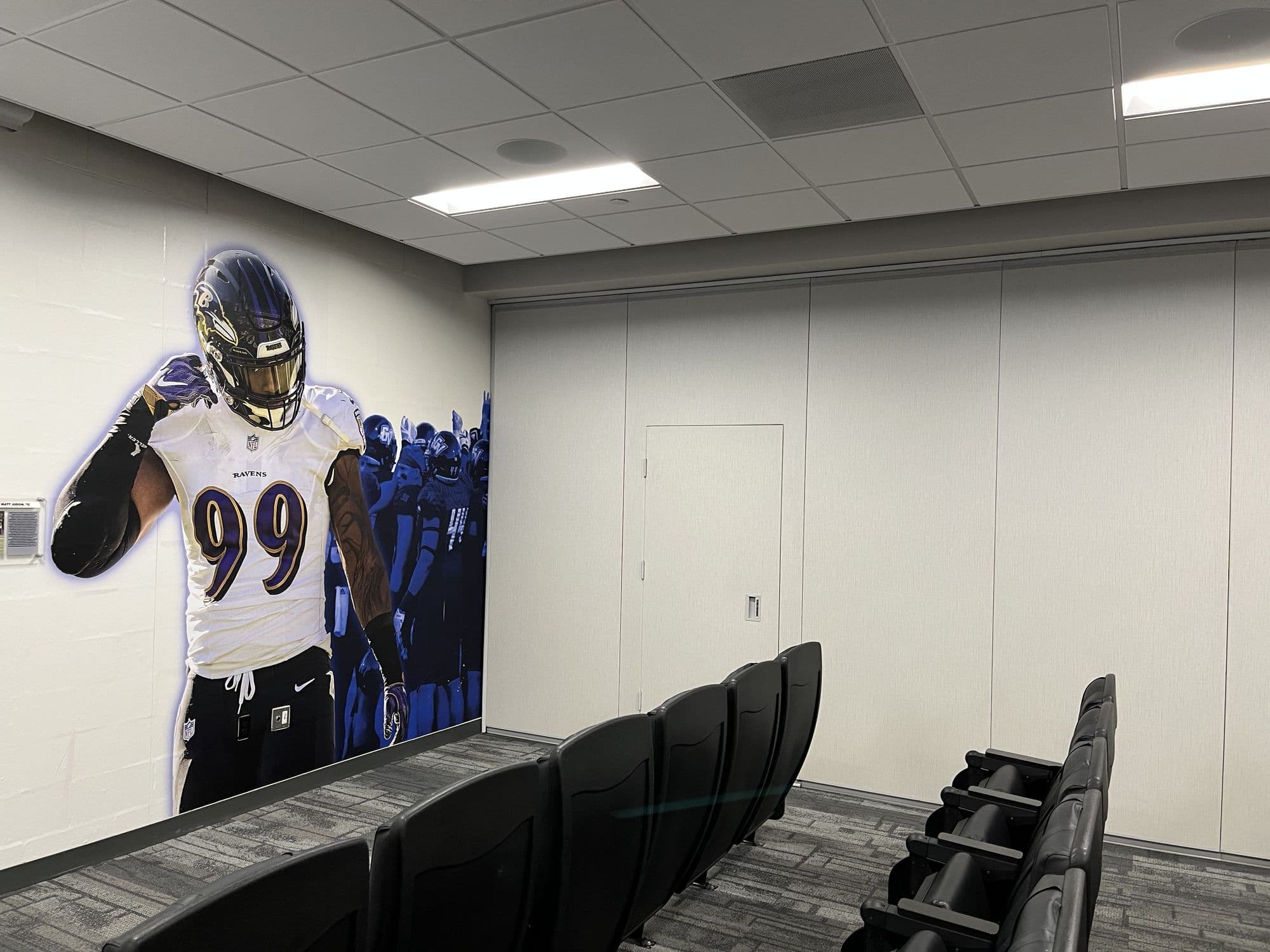Closed Modernfold Acousti-Seal partition with a pass door beside a player mural and theater seats in the GVSU film room