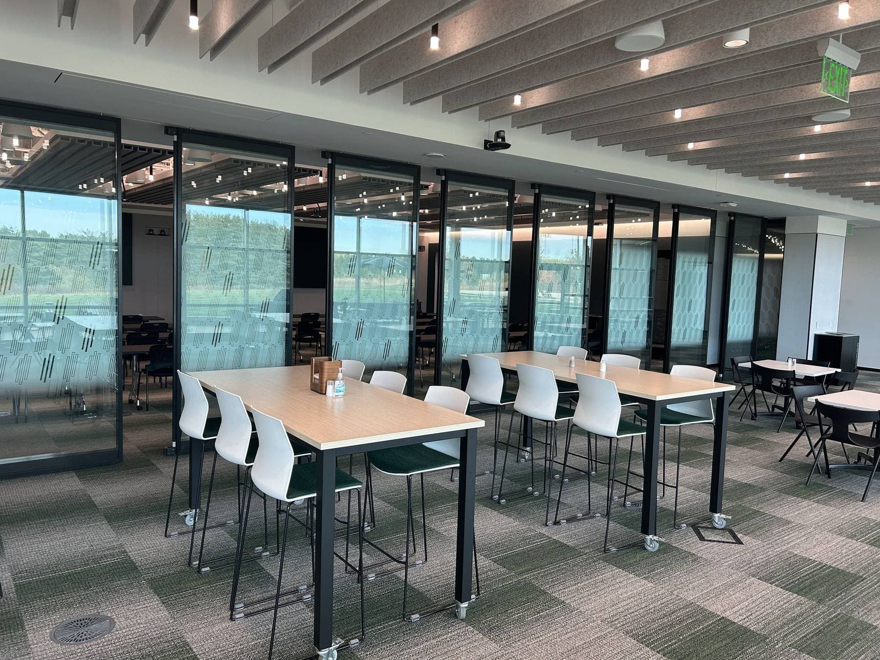 High-top tables and white stools in front of the closed Acousti-Clear glass wall
