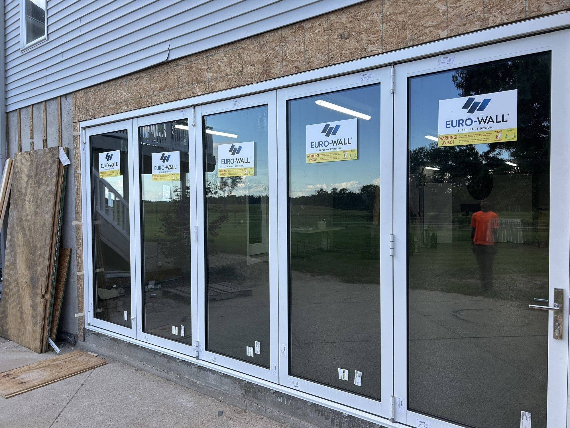 Close-up of the closed Euro-Wall folding glass panels with Euro-Wall labels on the glass and the hinged entry panel with its lever handle