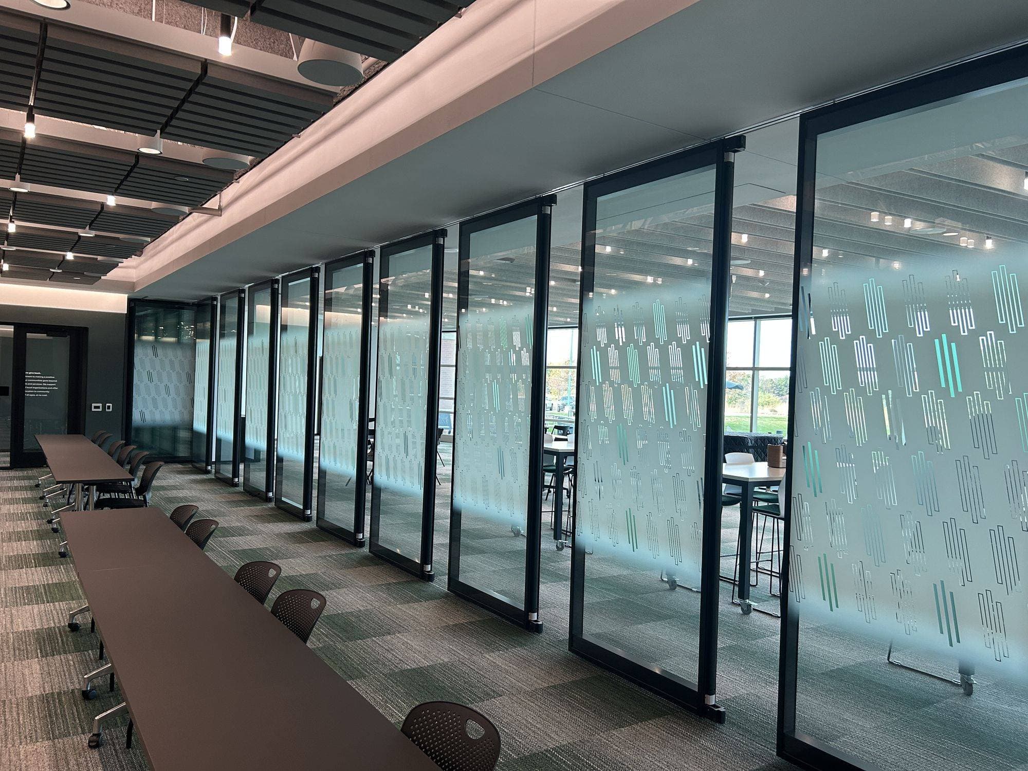 Closed Modernfold Acousti-Clear glass wall with a green and teal Creative Film pattern running beside long training tables at MSU Headquarters