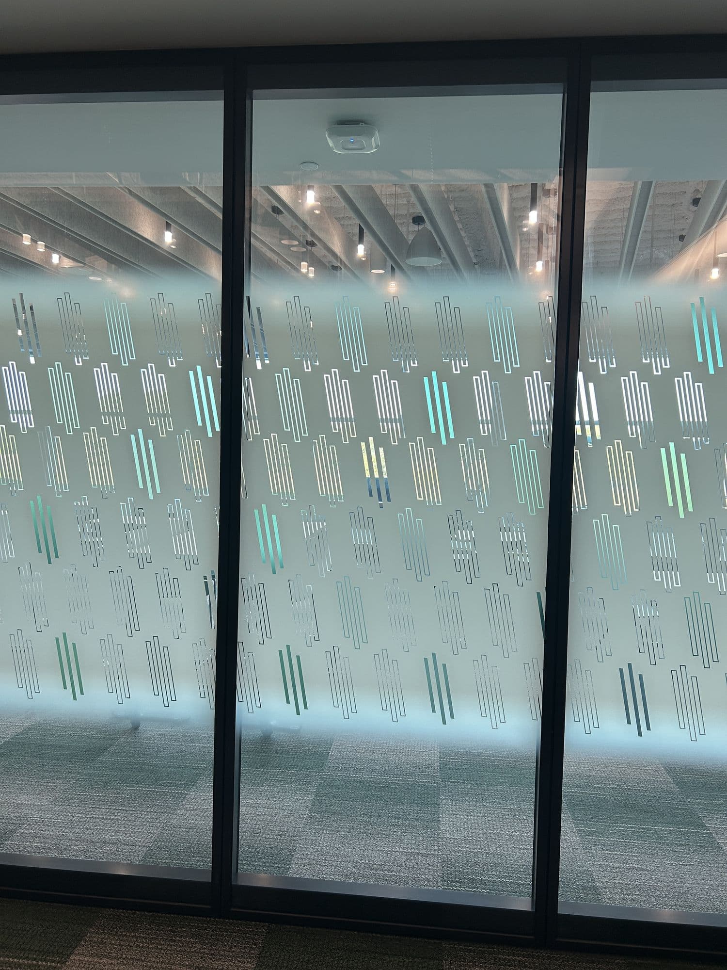 Close-up of Acousti-Clear glass panels with a green and teal Creative Film pattern and dark frames