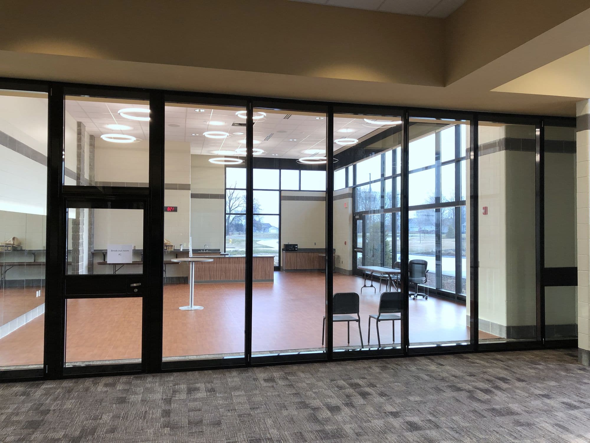Closed Modernfold Acousti-Clear glass wall with black frames and a pass door in the lobby at Zeeland East High School